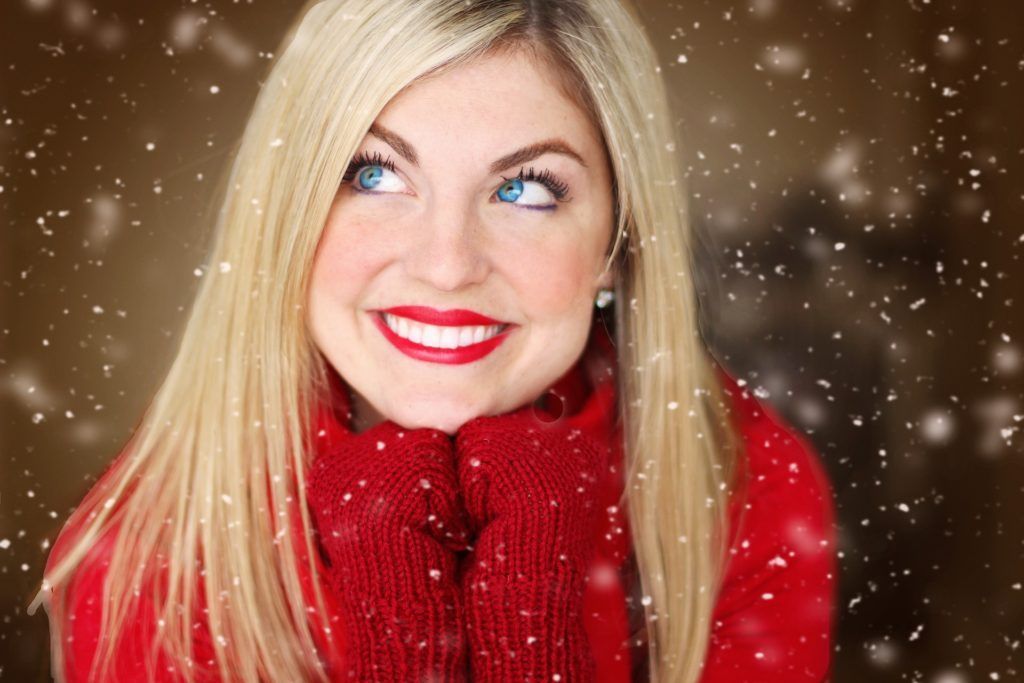A woman wearing a red sweater and red gloves is smiling in the snow.