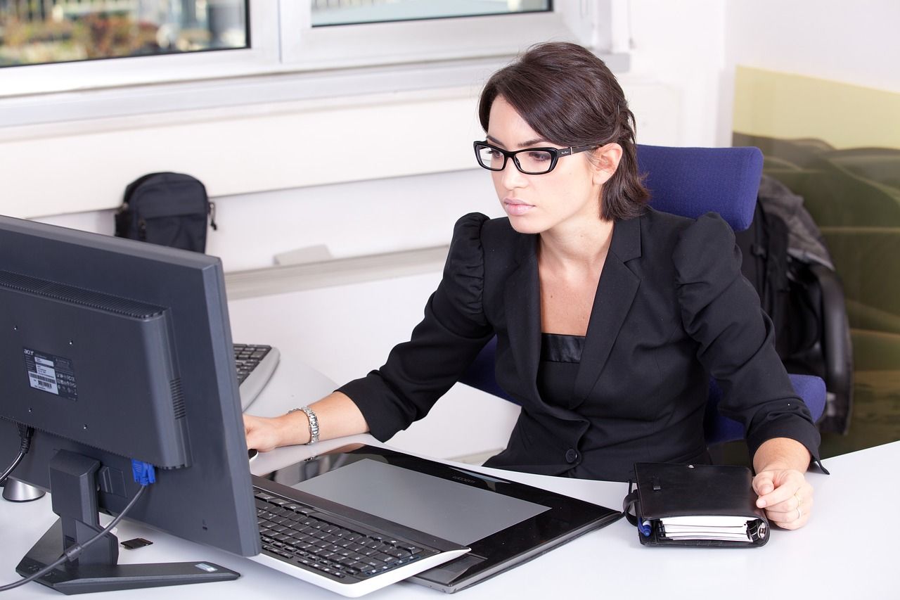 A woman wearing glasses is sitting at a desk in front of a dell computer