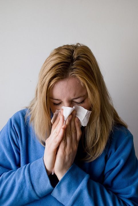 A woman in a blue sweater is blowing her nose with a napkin.