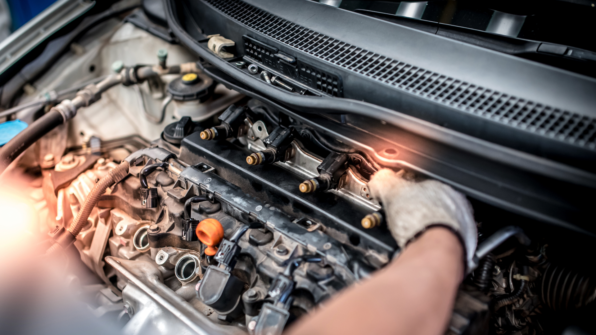 Mechanic working on car engine with tools, engine bay lit by bright orange sparks
