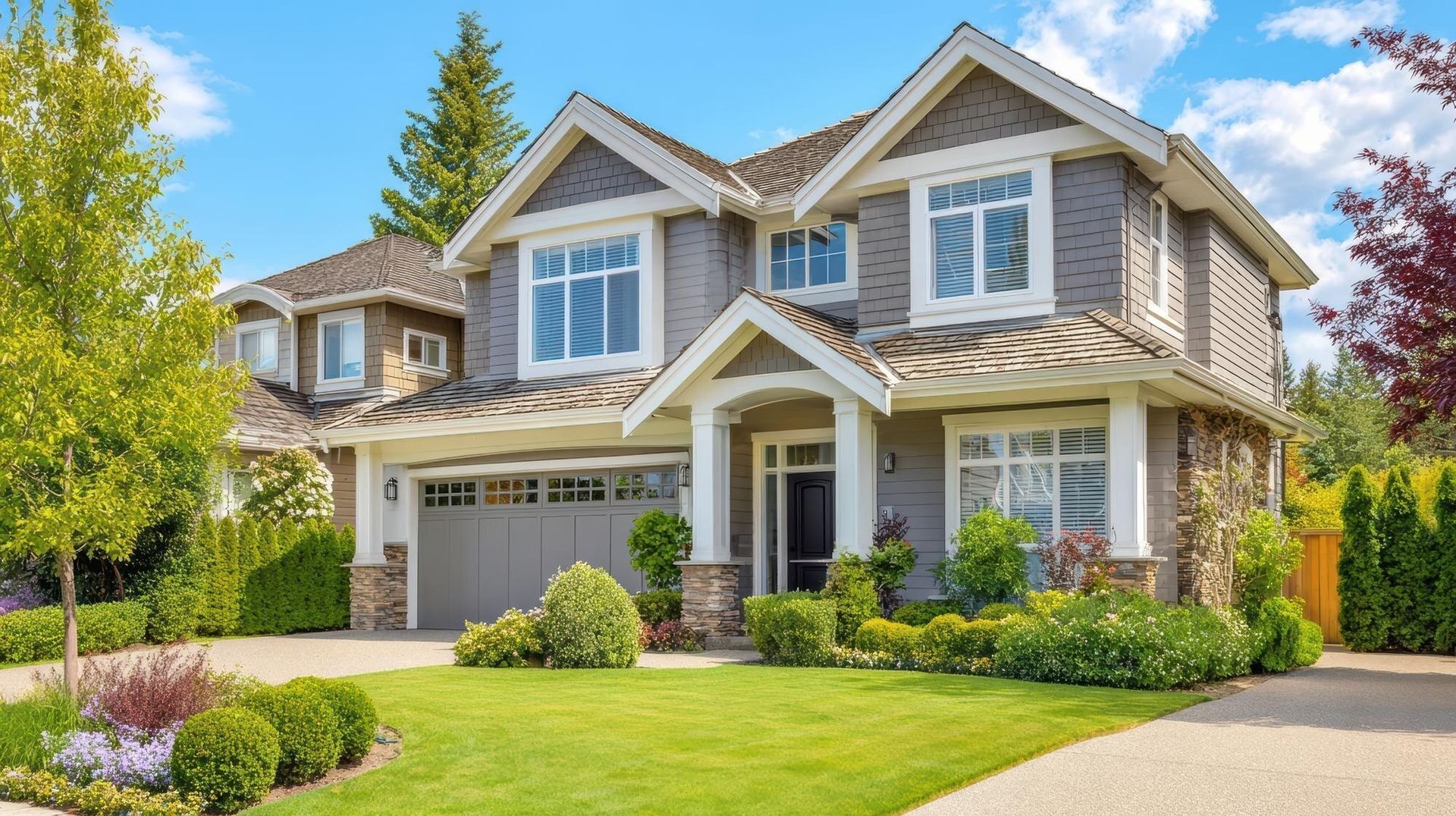 Two-story suburban house with gray siding, white trim, a garage, and a green lawn under a clear sky