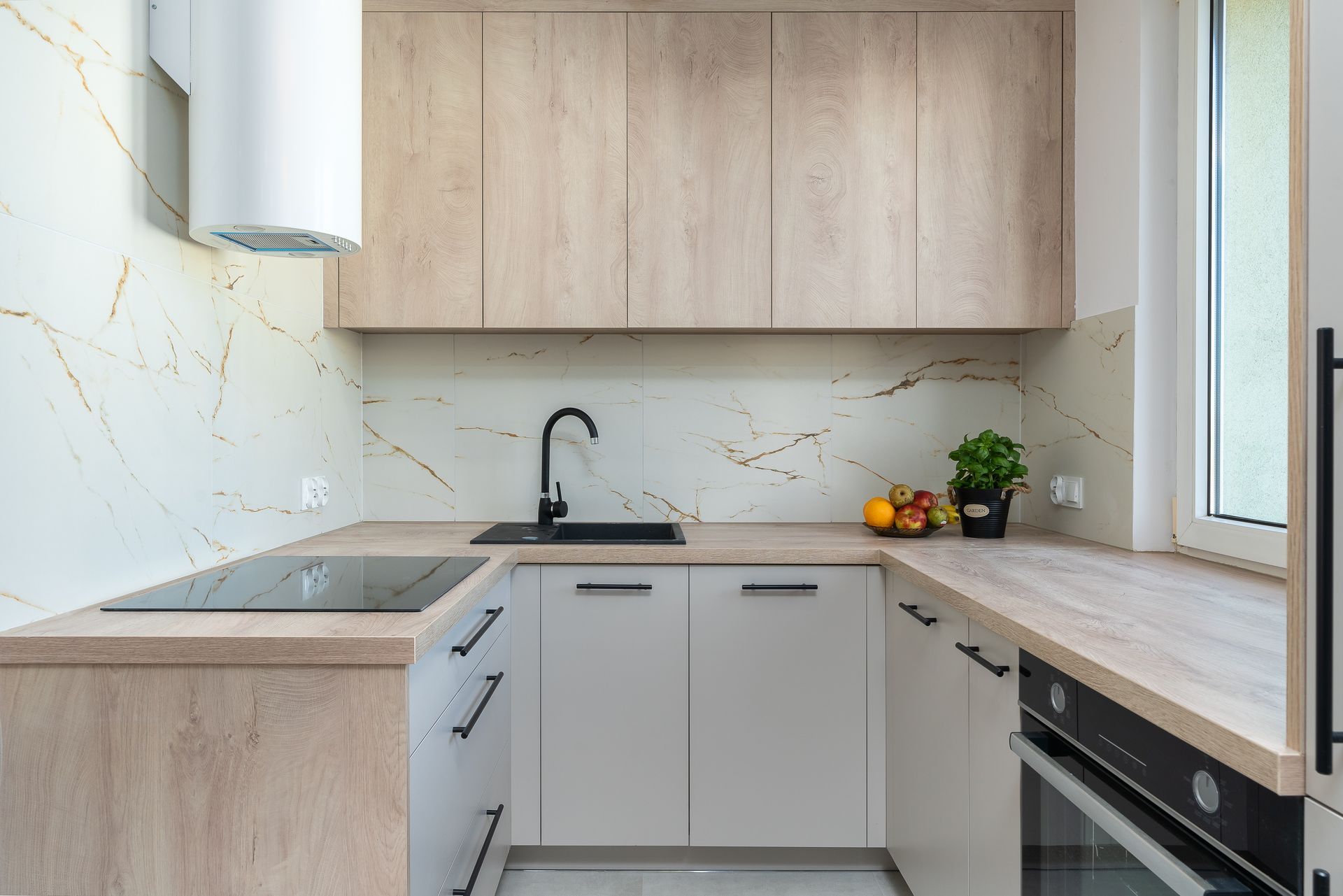 Modern compact kitchen with wood cabinets, white countertops, sink, stovetop, and built-in oven