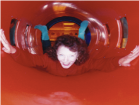Person sliding through a red tunnel slide, smiling with arms outstretched
