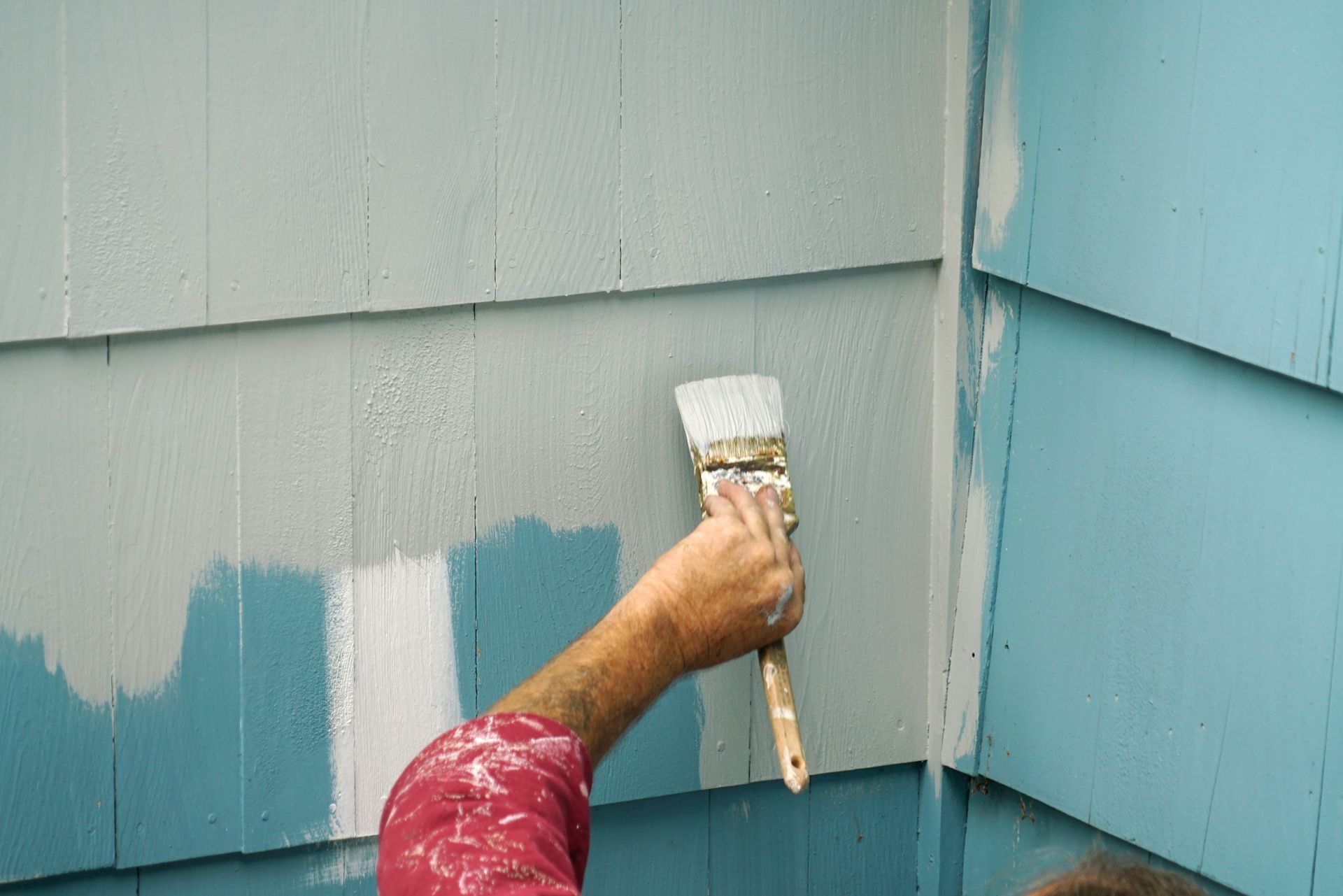 Close-up of a hand painting exterior wood siding with a brush. Close-up of a hand painting exterior wood siding with a brush.