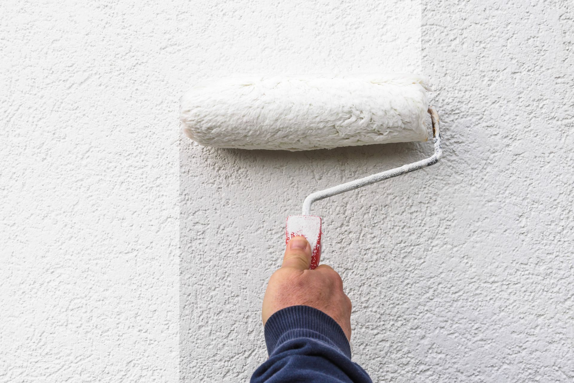 Painter's hand holding a roller filled with paint.