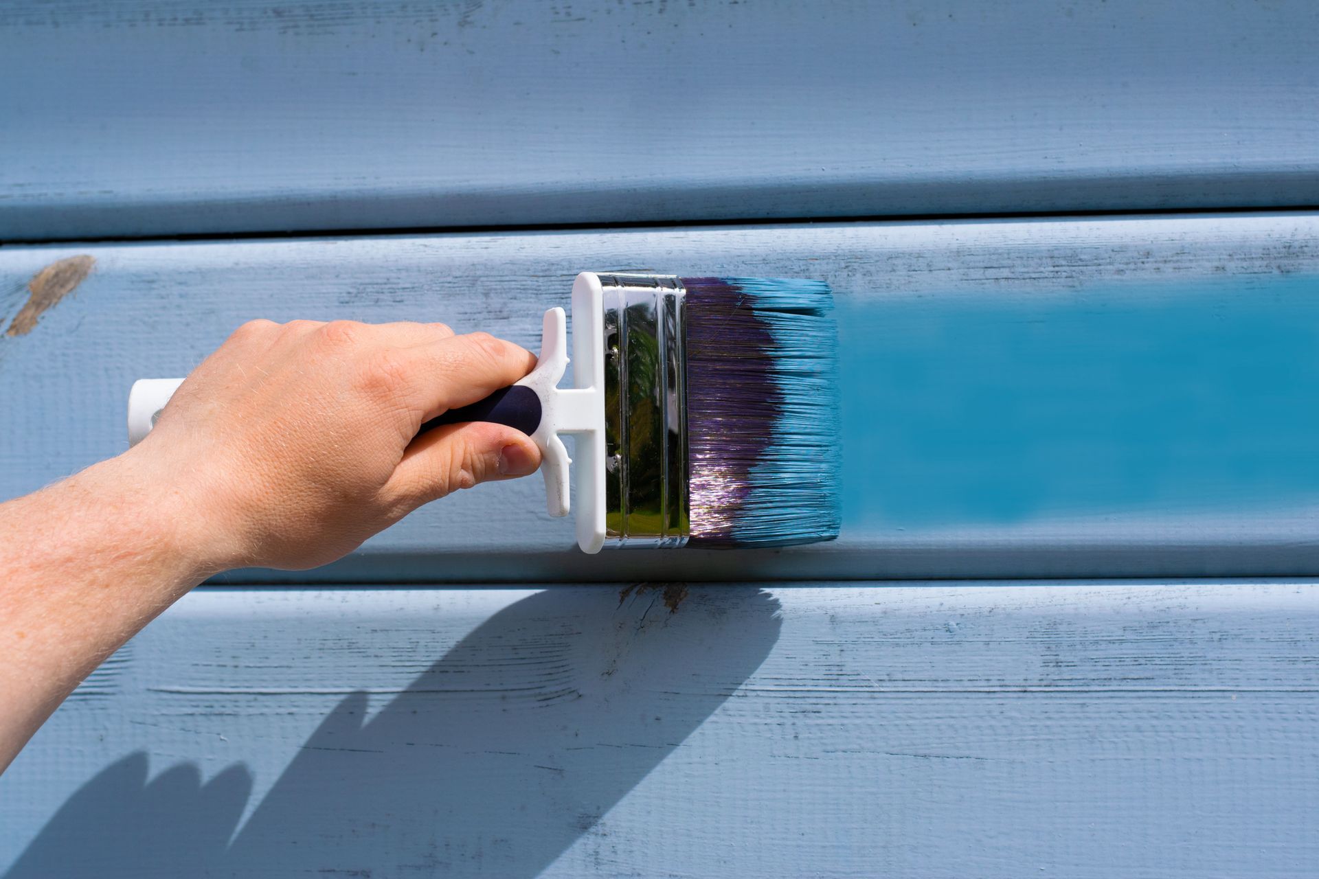 Hand with blue paint brush on the wooden wall.