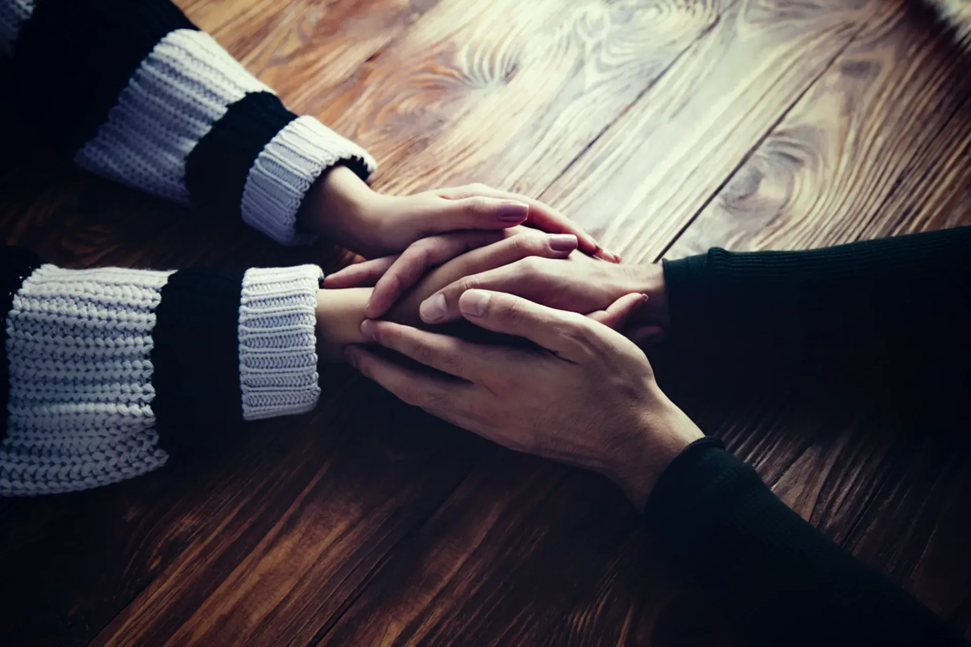 Two hands clasped together on a wooden table, sleeves in black and white.