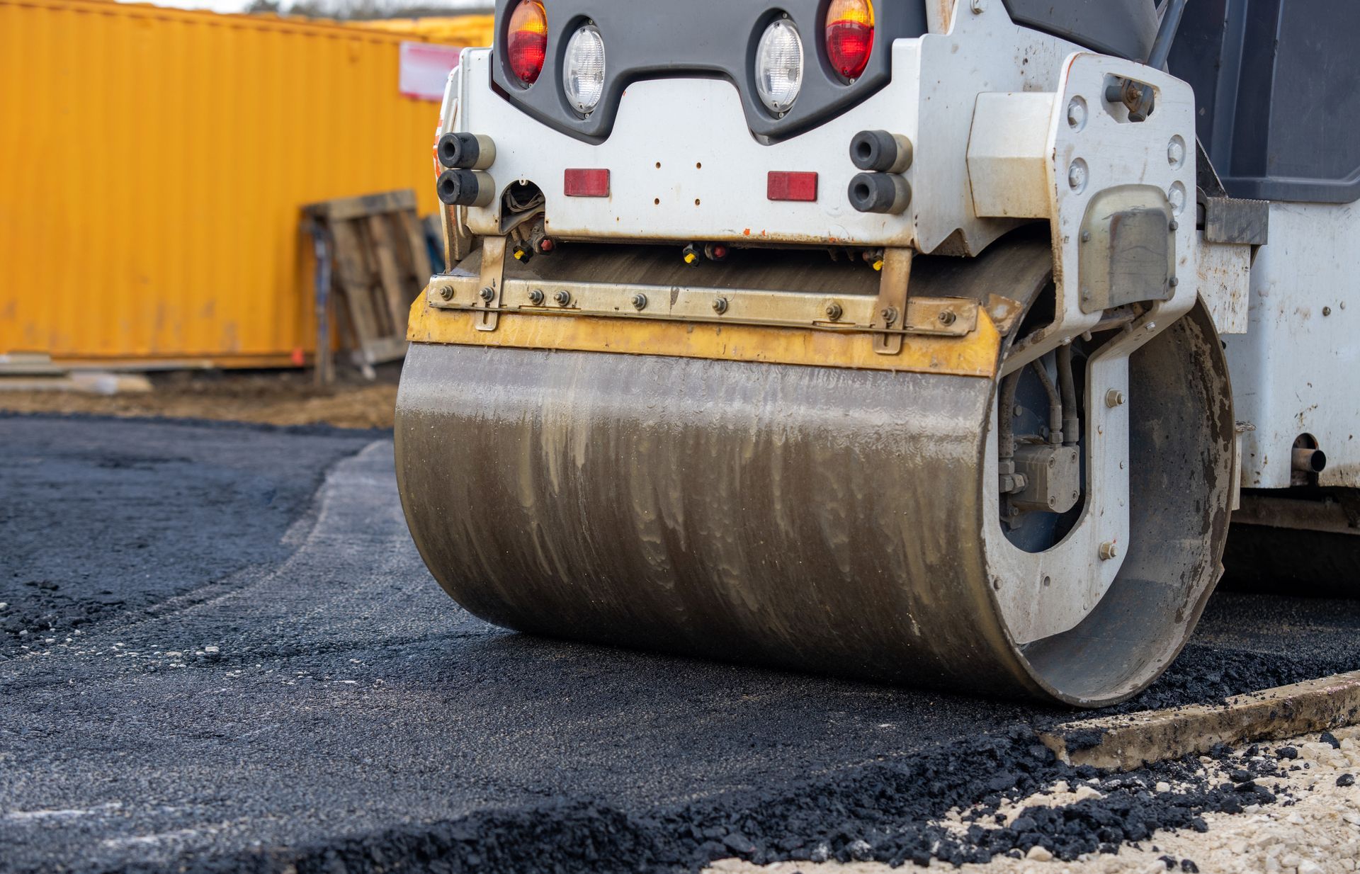 Road roller compacting fresh asphalt beside a yellow container Road roller compacting fresh asphalt beside a yellow container