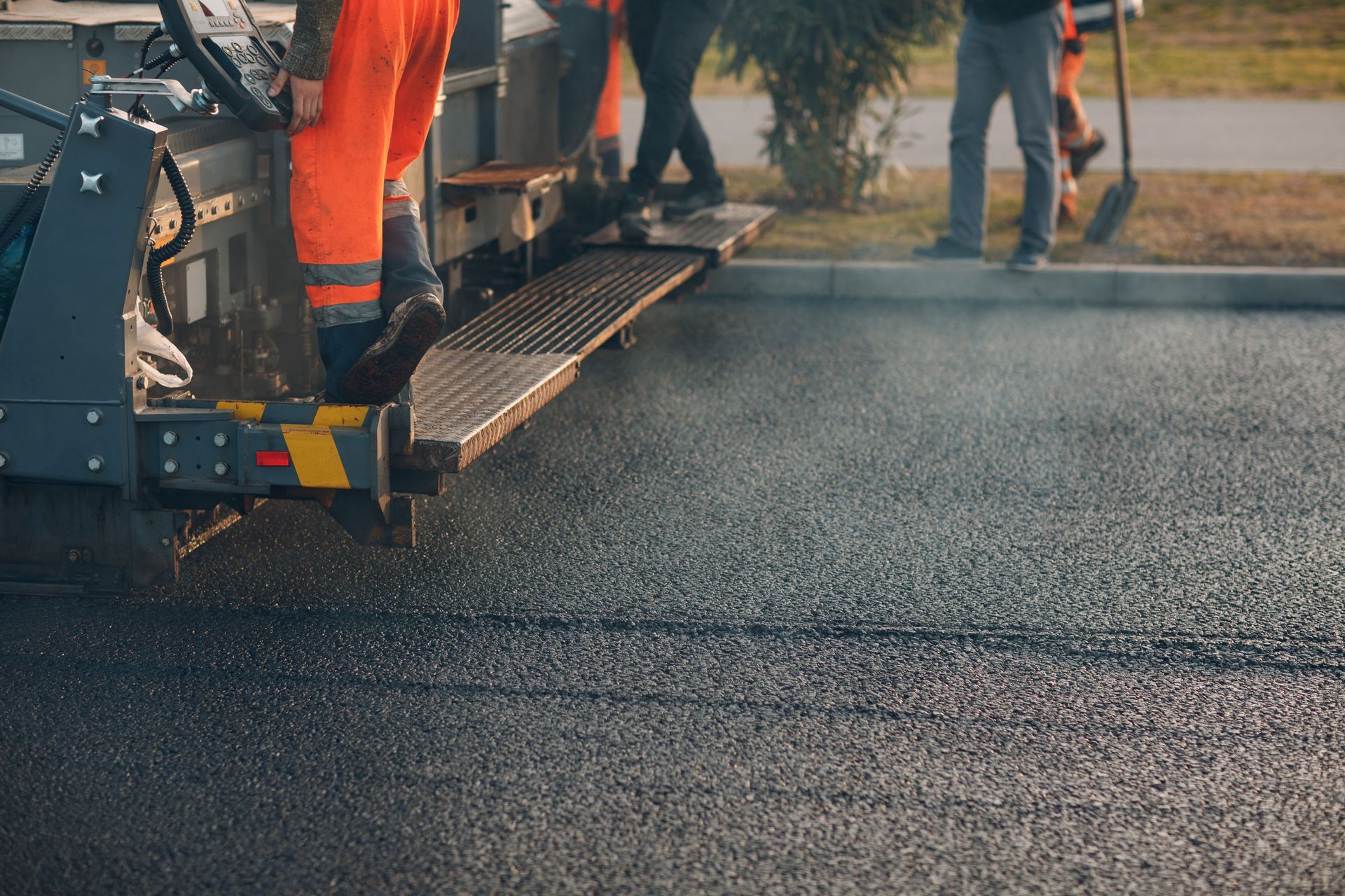 Workers paving a road with asphalt using heavy machinery.
