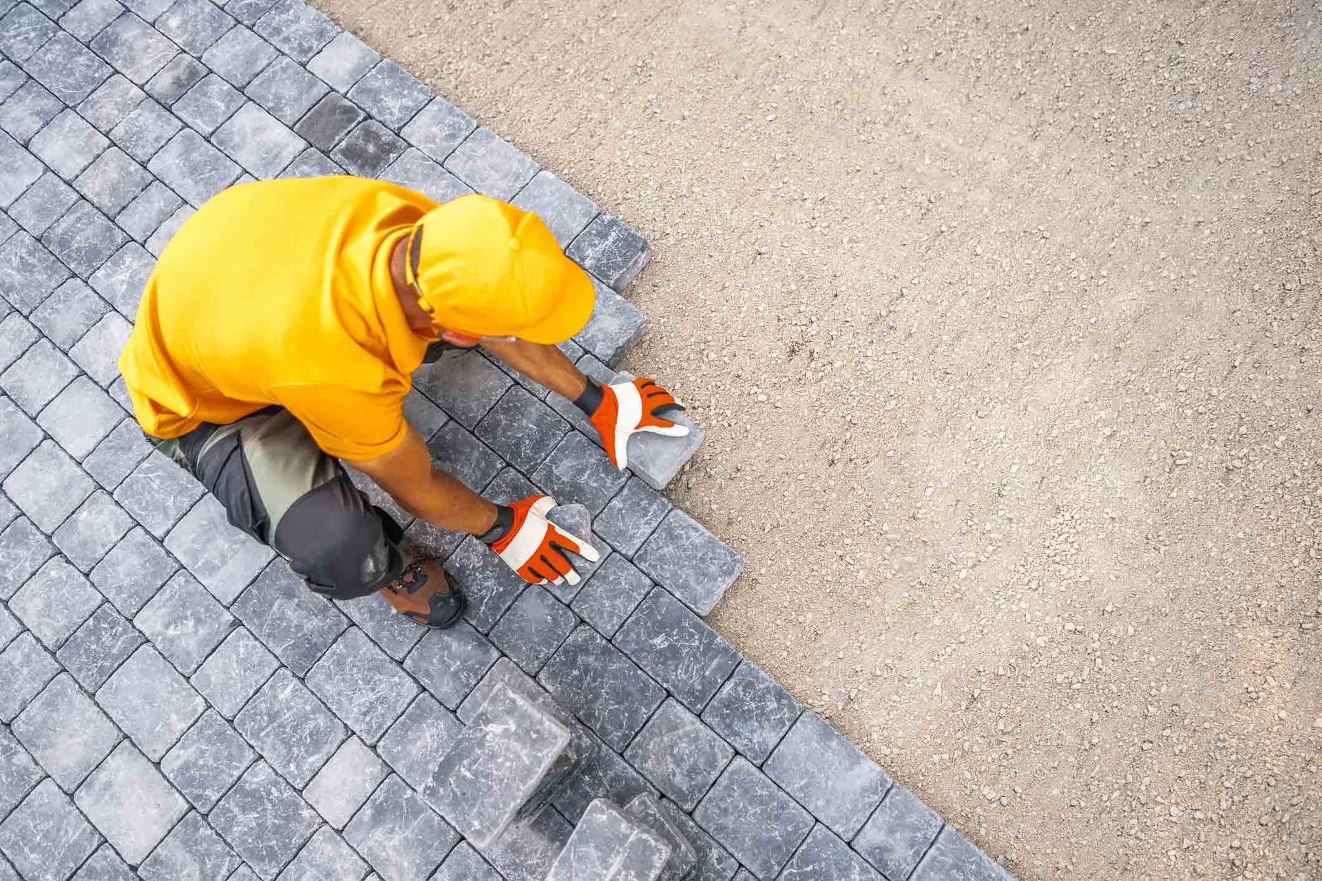 A man is laying bricks on a driveway.