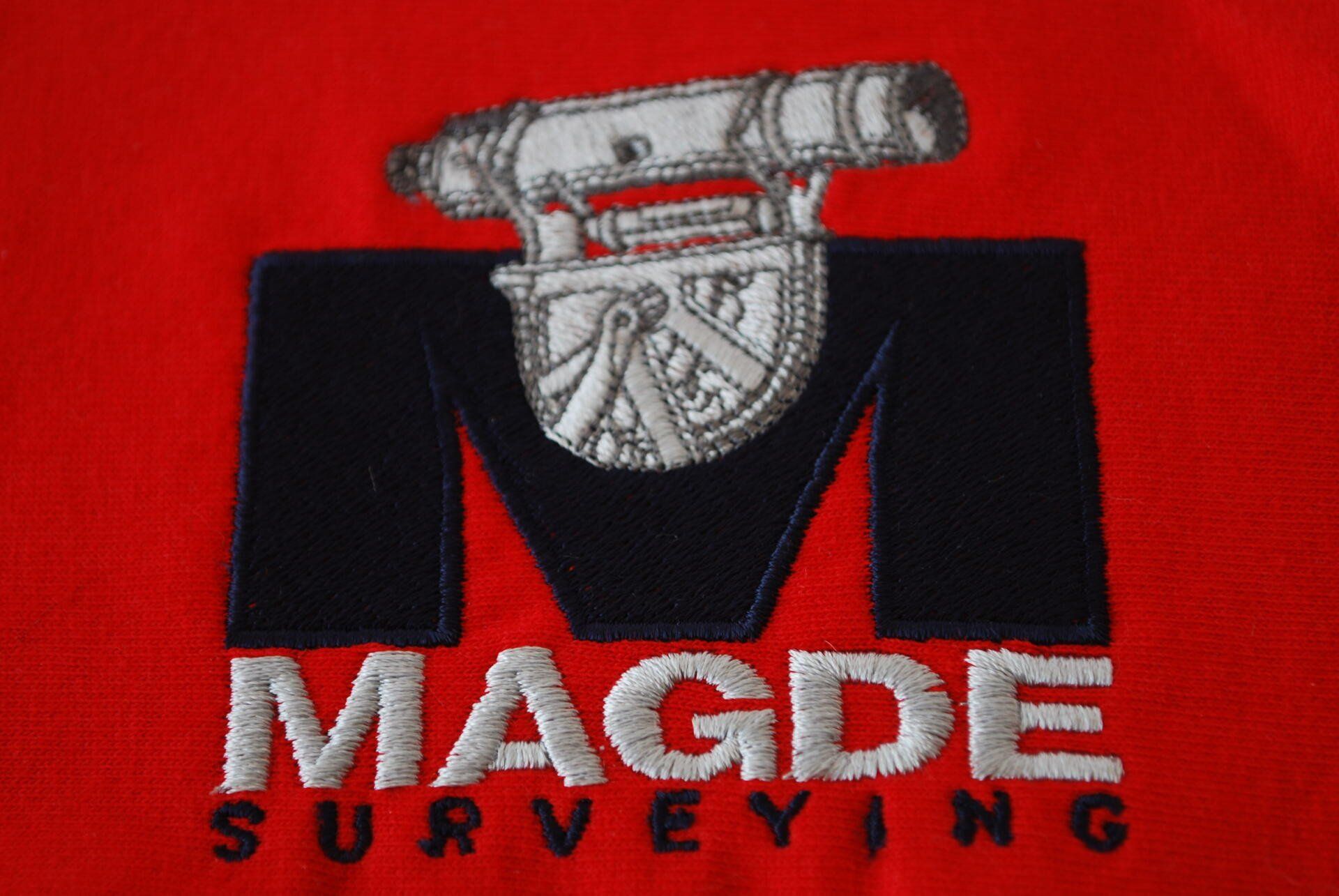 A red shirt with the Magde Surveying logo embroidered on it