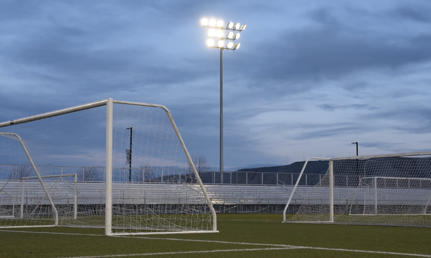 Soccer field with goalposts under bright stadium lights at dusk, cloudy sky overhead