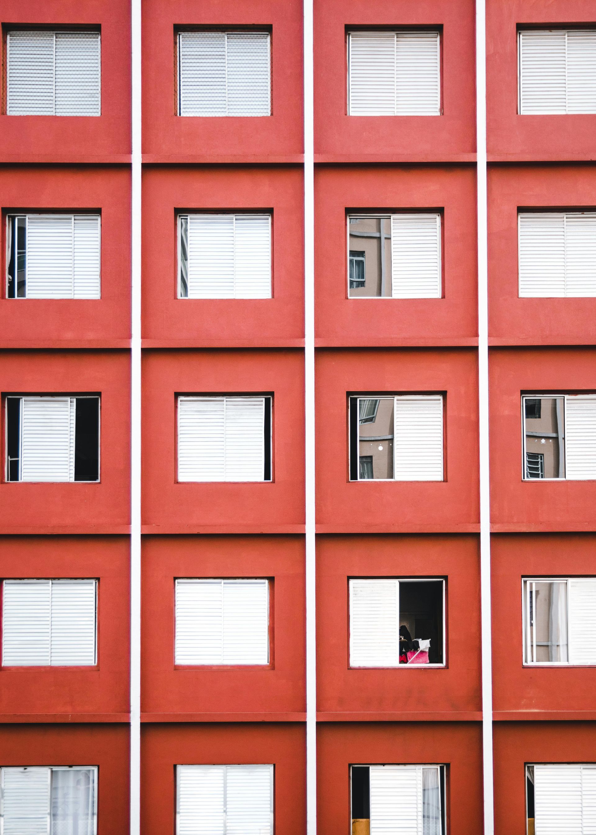 Red apartment building facade with rows of windows and white shutters