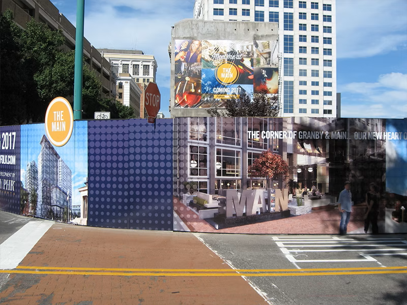 Construction site with colorful advertising panels. A crosswalk is in the foreground. Buildings in the background. Construction site with colorful advertising panels. A crosswalk is in the foreground. Buildings in the background.