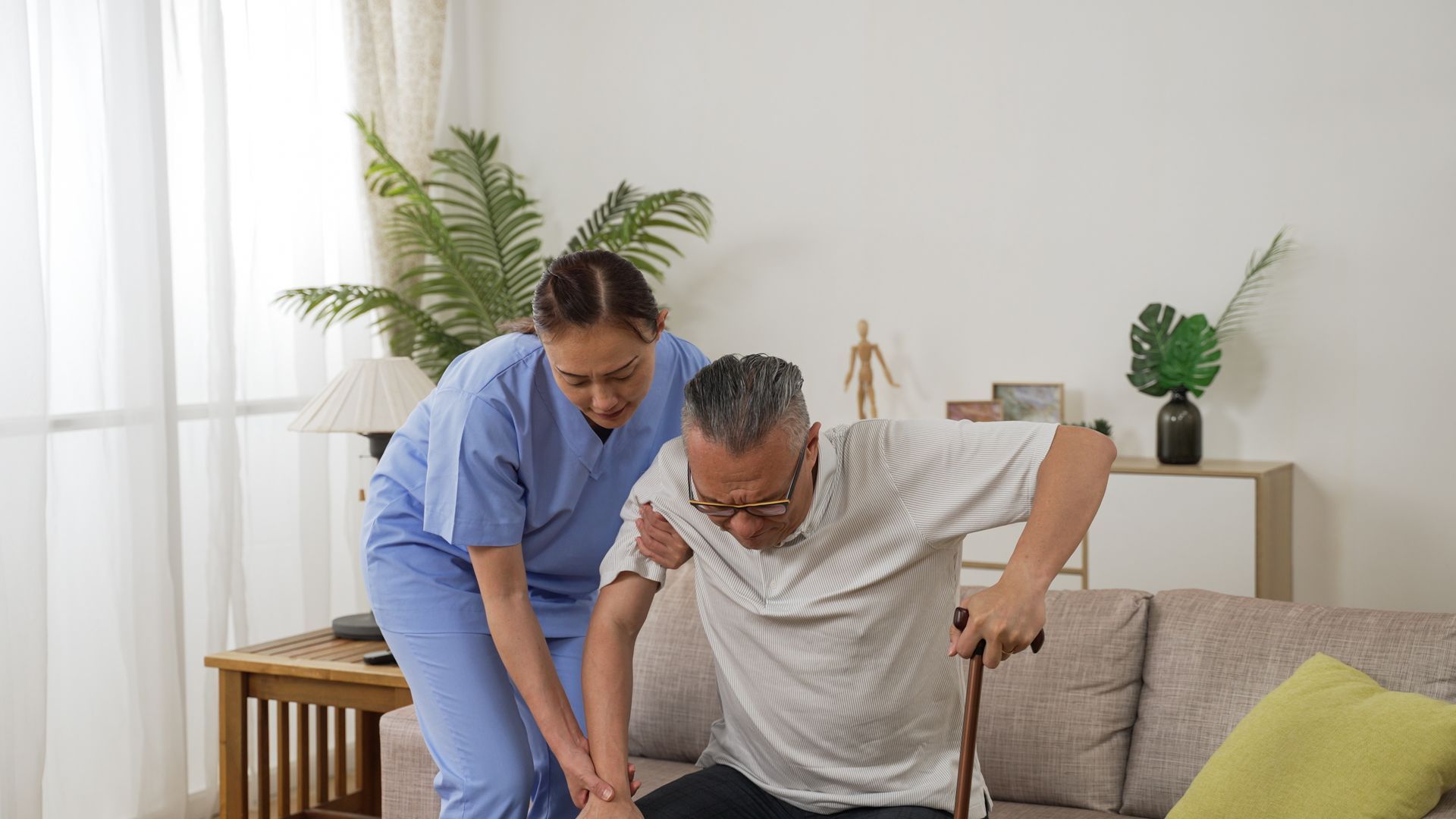 A caregiver is helping a senior man to stand up.