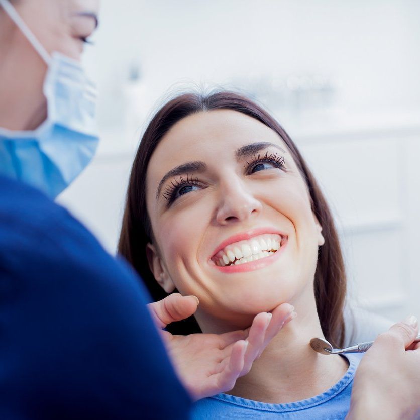 A woman is smiling while having her teeth examined by a dentist.