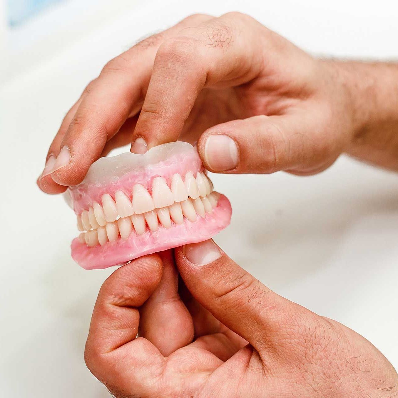 Dental technician holding artificial teeth arrangement of full mouth complete denture 
