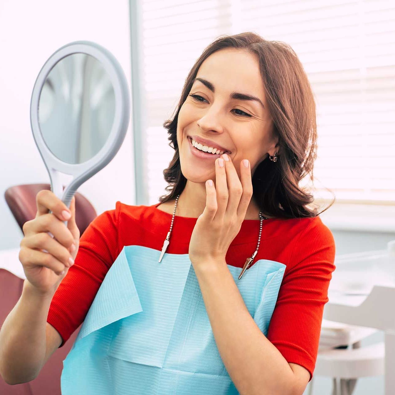 Pretty girl in dentist cabinet is using a mirror