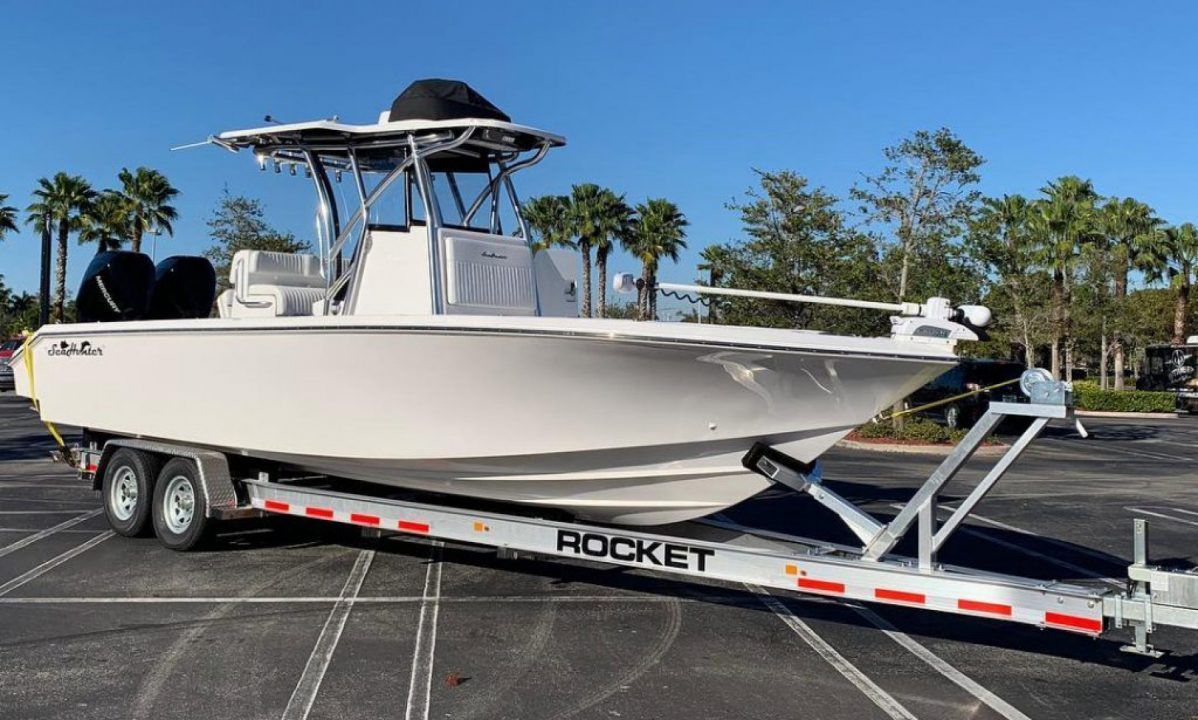 White center-console boat on a trailer in a sunny parking lot, with palm trees in the background