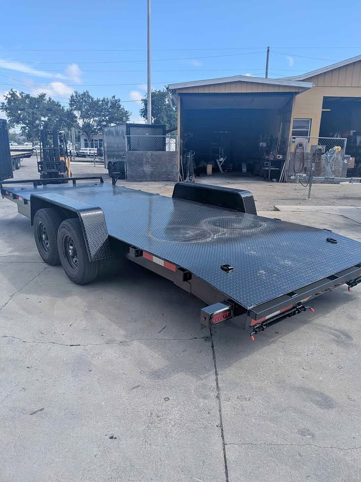 Black flatbed trailer parked outside with an open ramp at a warehouse or industrial lot