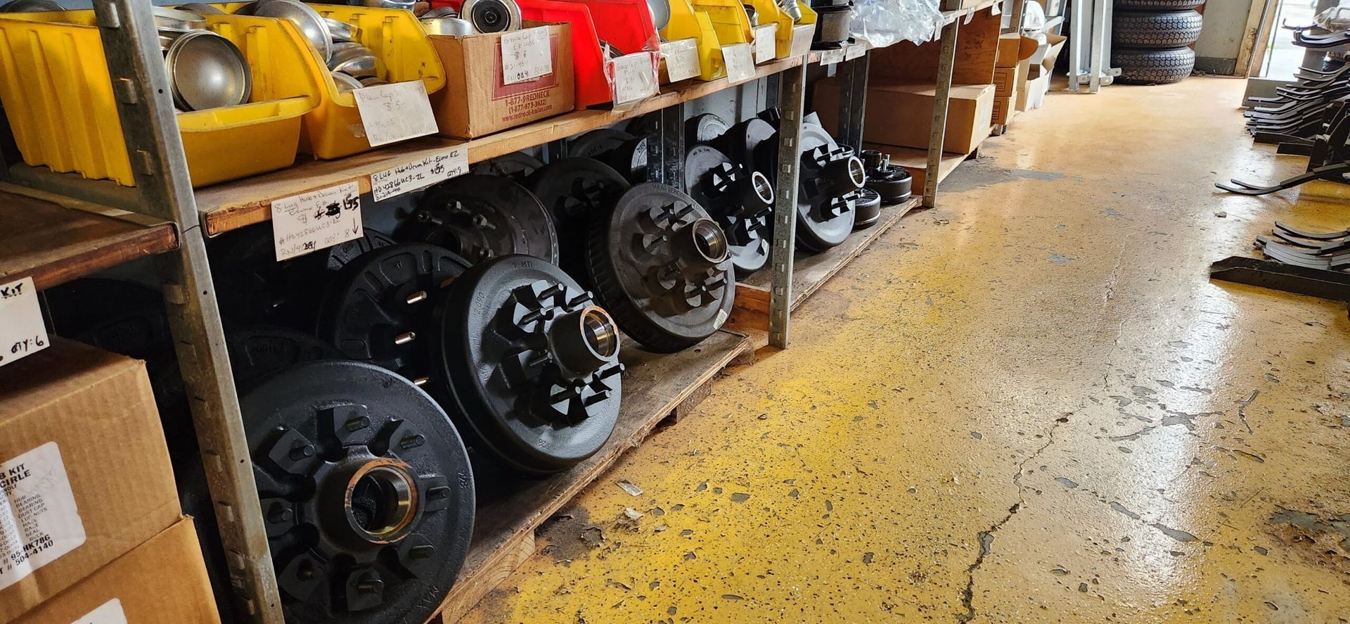 Tire shop aisle with stacked black wheels, yellow equipment, and shelves along a concrete floor