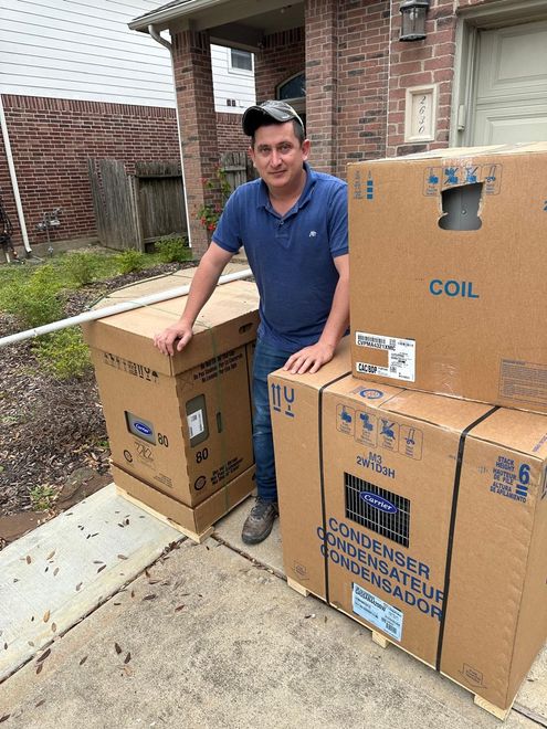 Picture of the owner of precise plumbing and air standing in between cardboard boxes. 