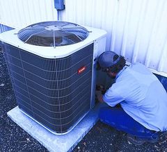 HVAC technician in red shirt, kneeling, attaching gauges to an AC unit outside a brick building. HVAC technician in red shirt, kneeling, attaching gauges to an AC unit outside a brick building.