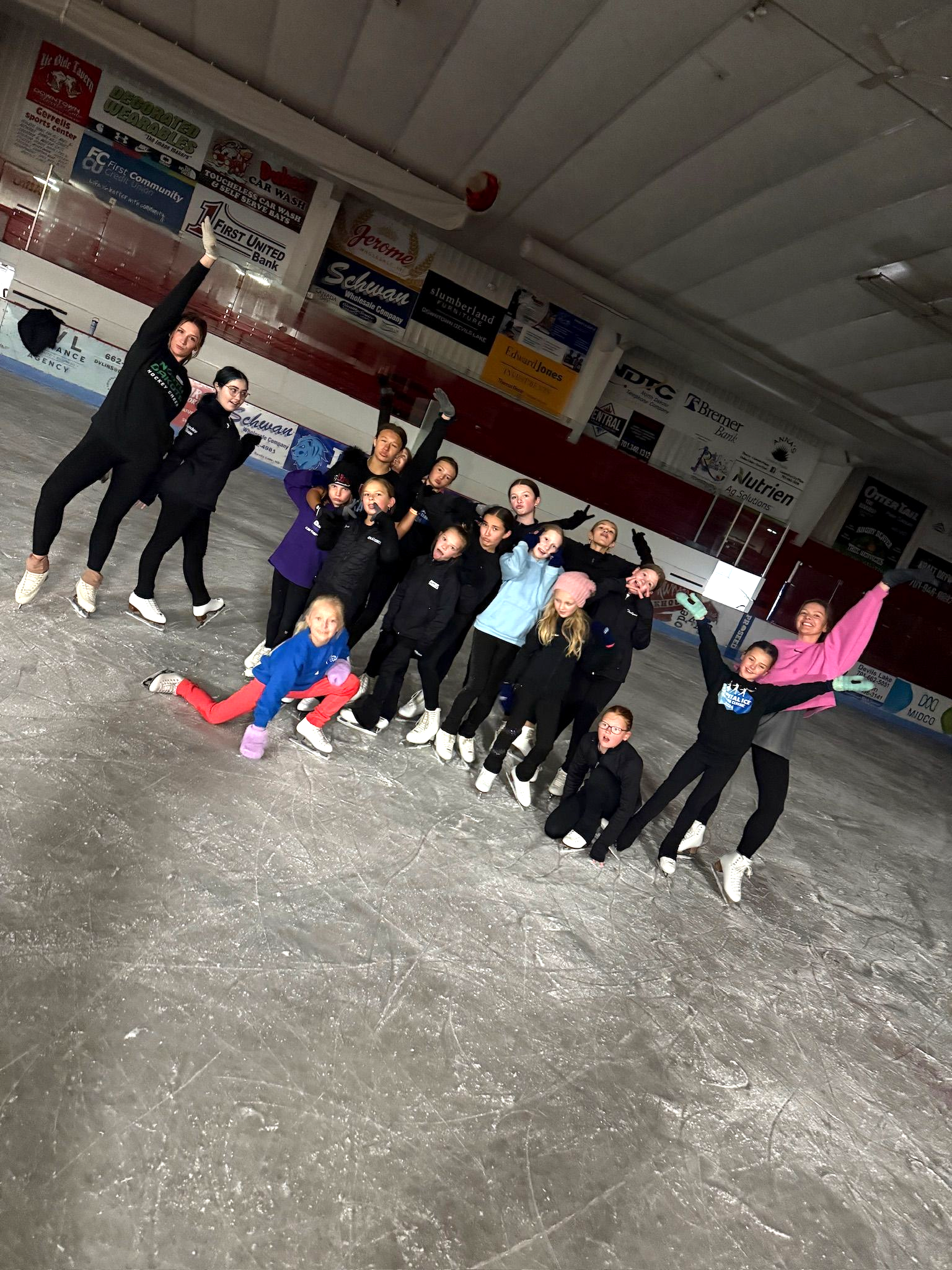Group of people posing on an indoor ice rink, with one person in bright pink and red standing out.