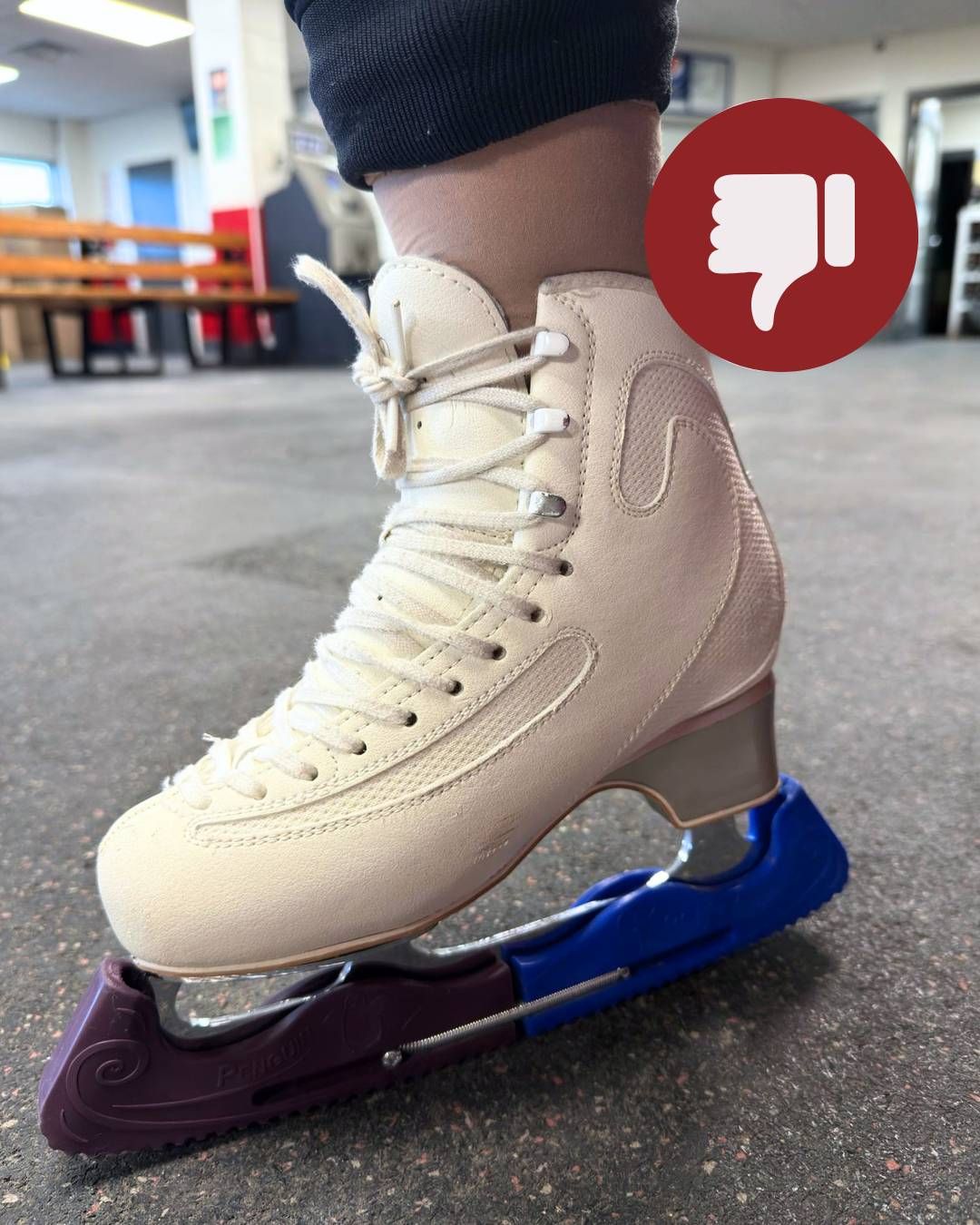 White figure skate on a blue and purple blade guard, worn on an indoor rink floor.
