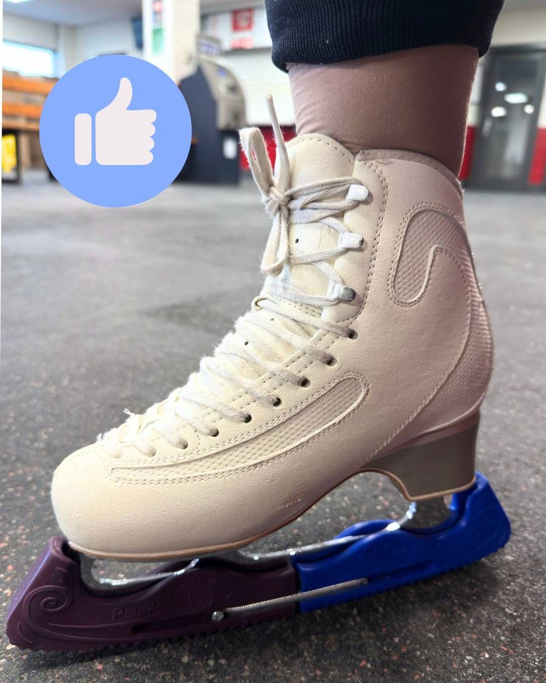 Beige figure skate with blue and maroon blade guards on ice or rink floor, close-up view