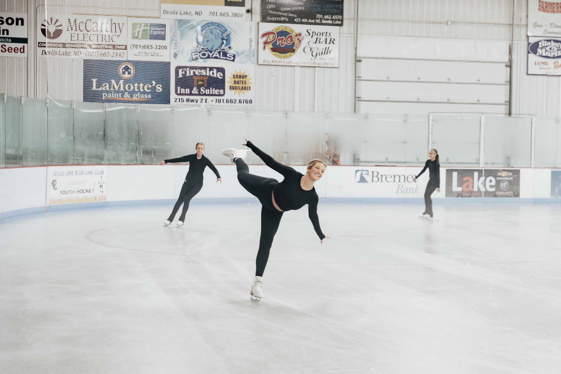 Three figure skaters on an ice rink, the center skater in a graceful pose.