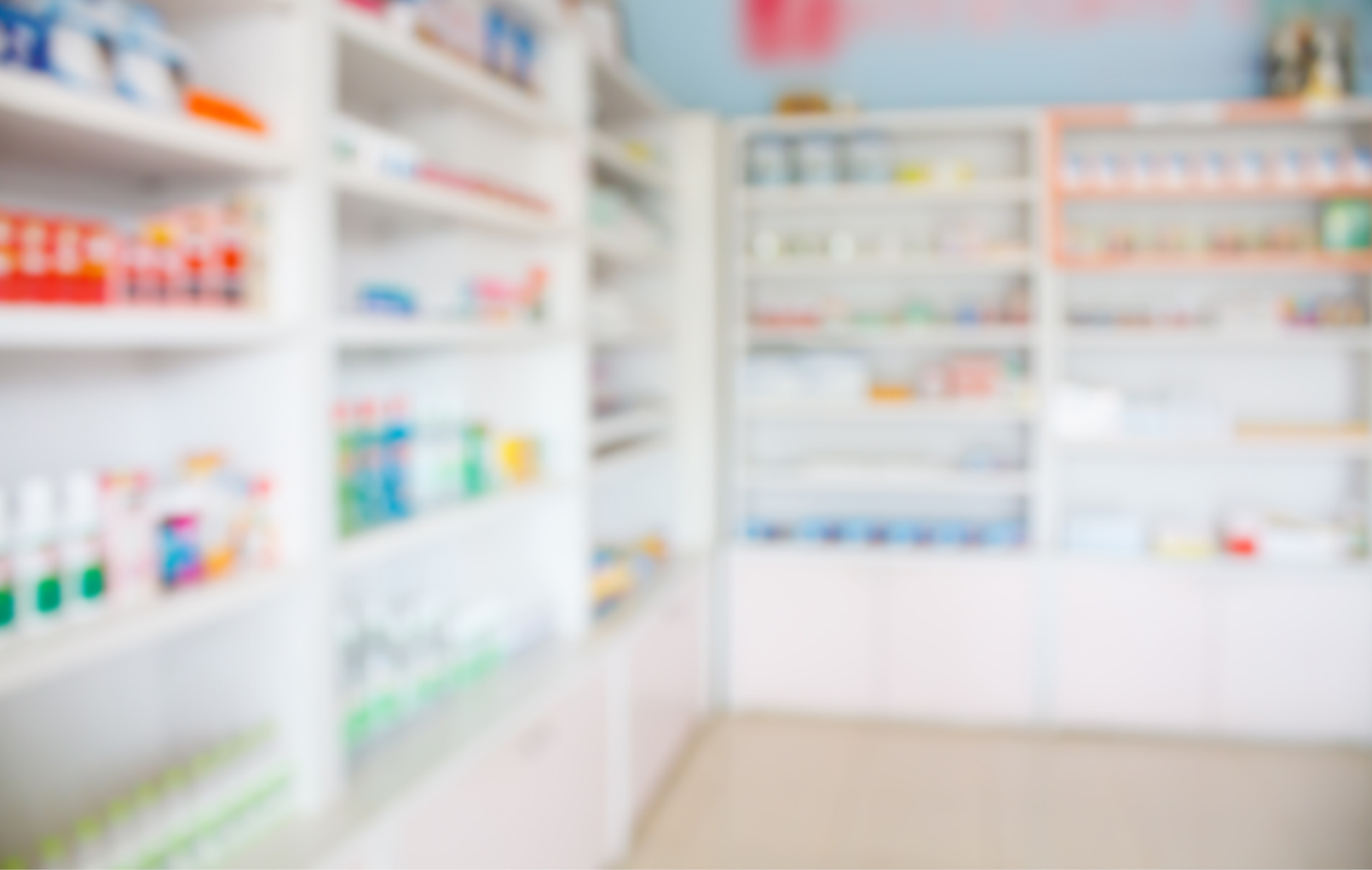 Blurred view of the white shelves of a pharmacy filled with various medicine containers and products.