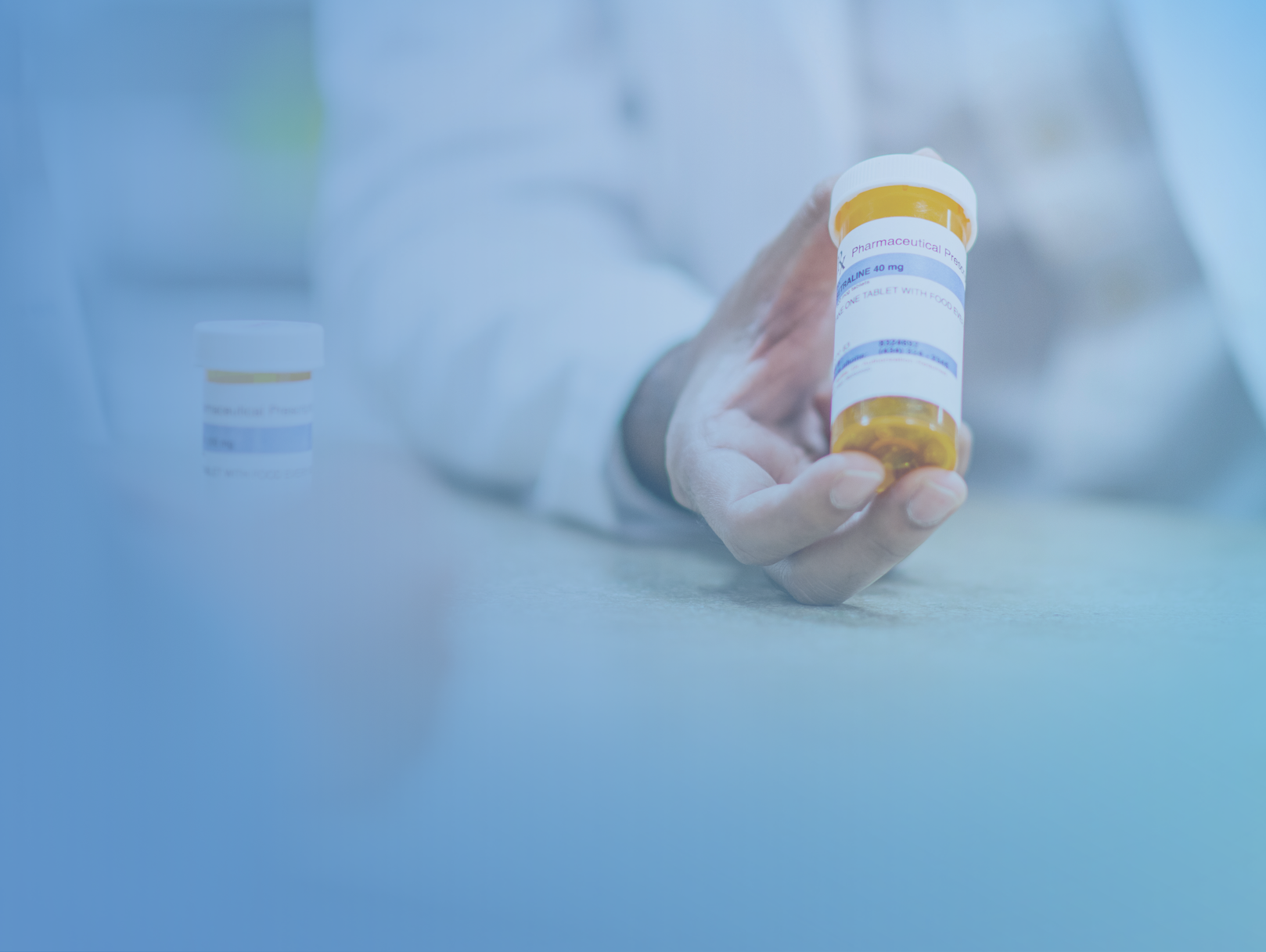 A person in a white lab coat holds a prescription medicine bottle, with another small container visible on the table.