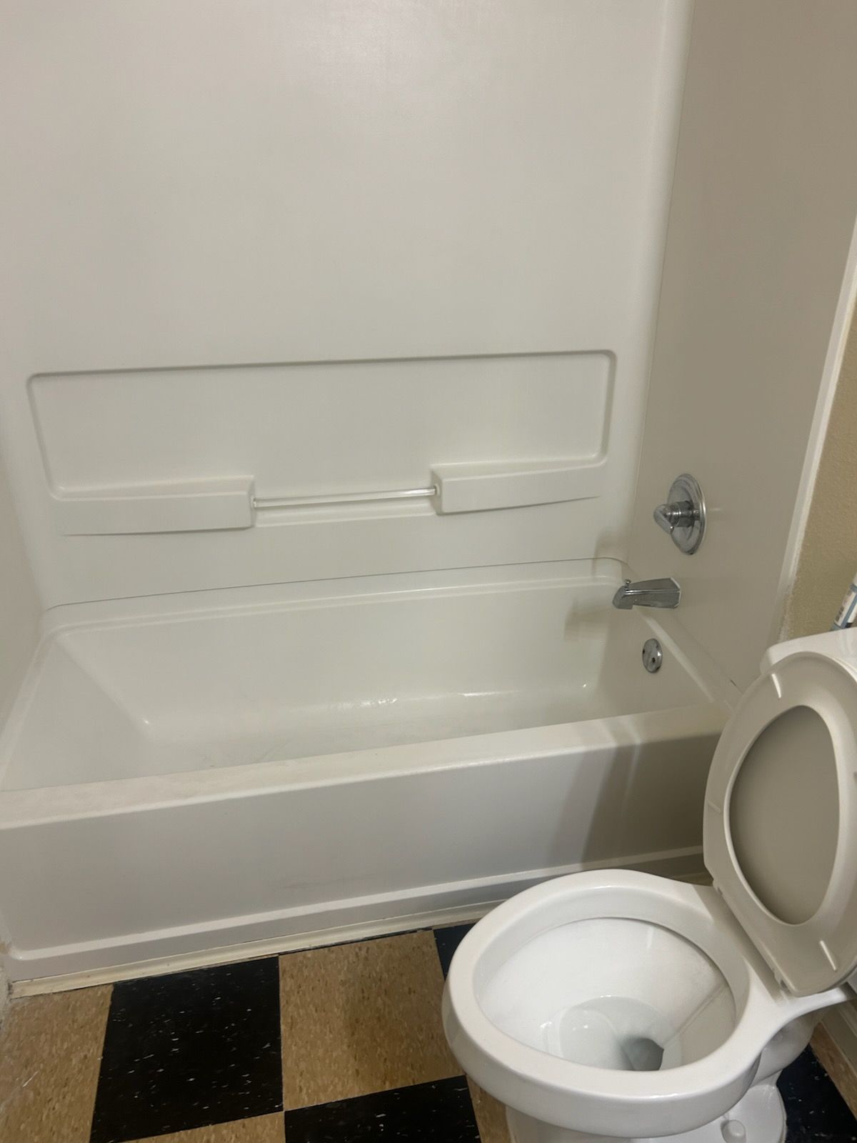 A white bathtub with built-in shelves next to a toilet, set against a black and cream checkerboard floor.