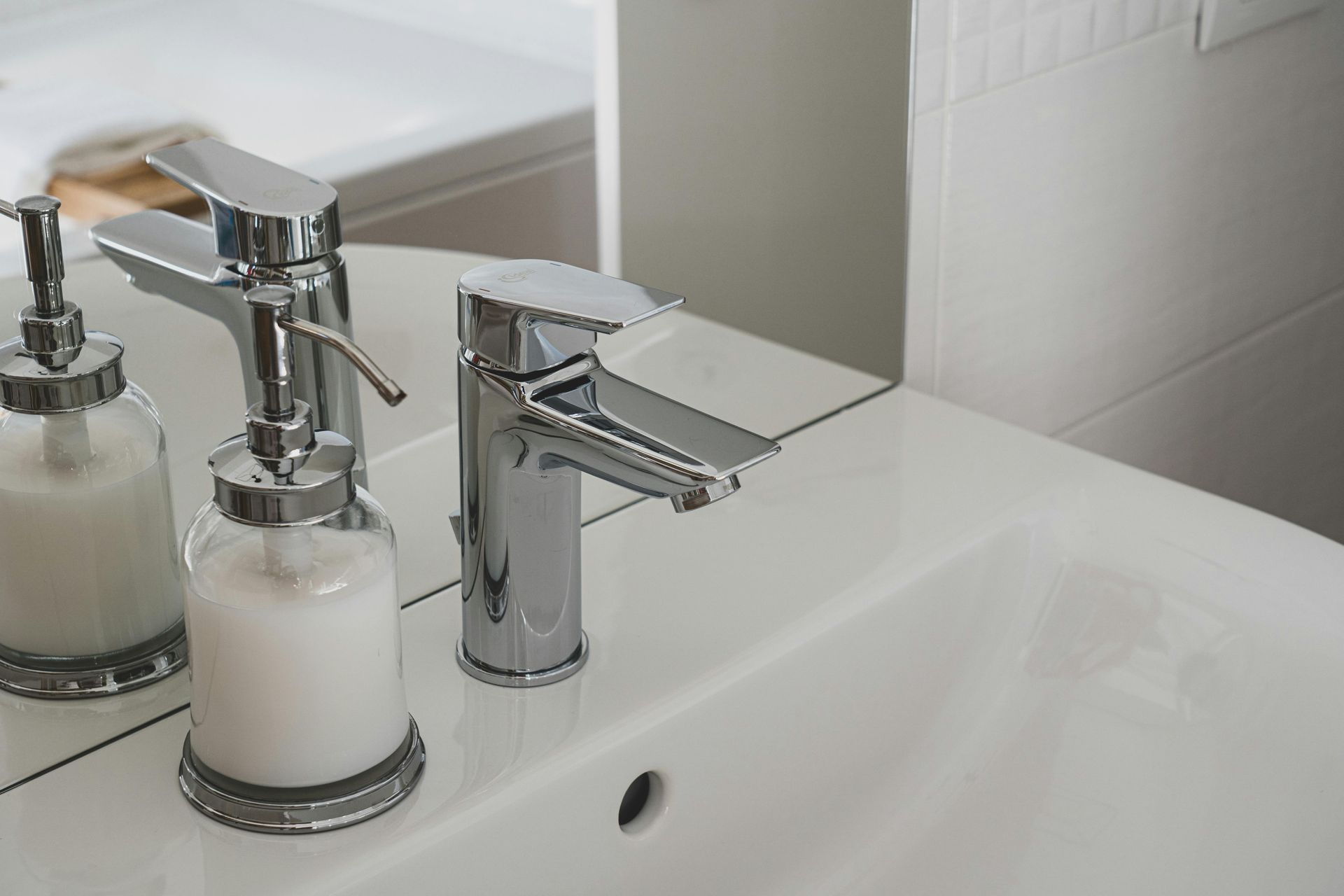 A modern chrome faucet and a glass soap dispenser on a white bathroom vanity sink.