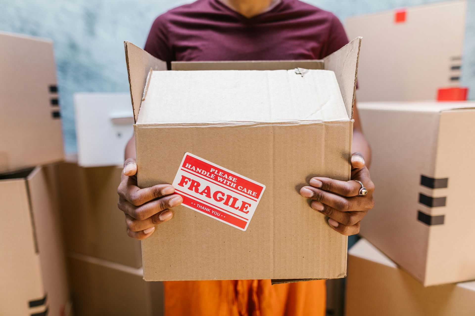 A person wearing a maroon shirt holds a brown cardboard box with a red