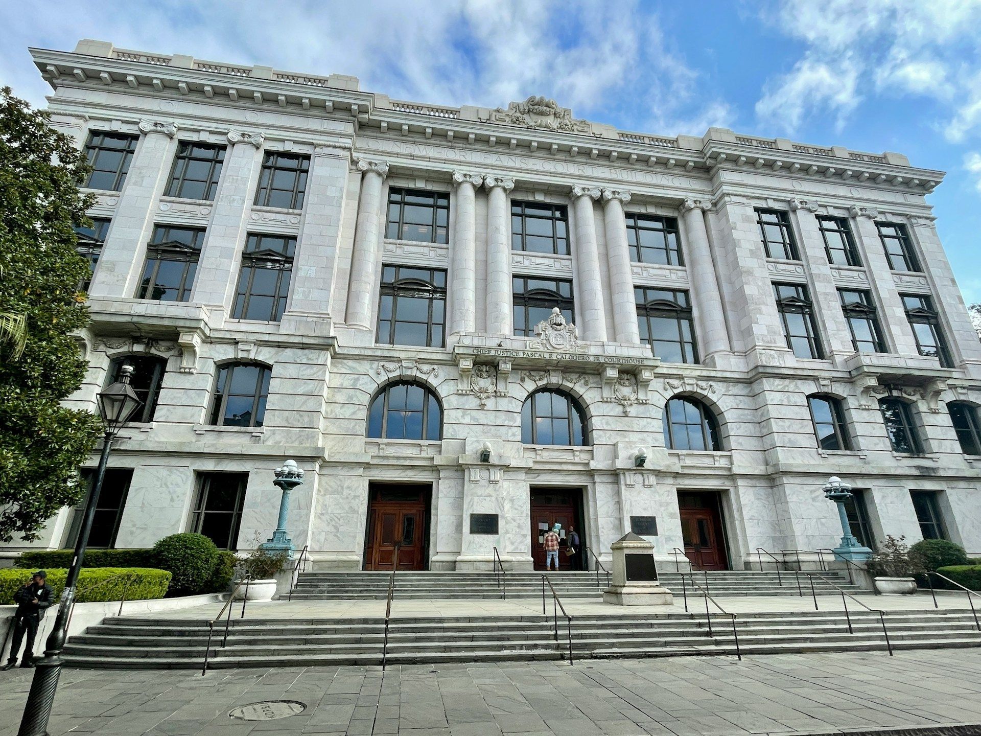 Beige courthouse with columns and steps, under a cloudy sky.