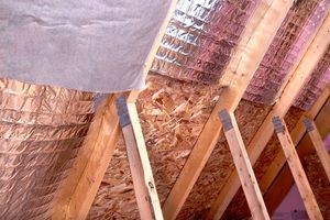 Wooden rafters with metallic insulation in an attic setting.