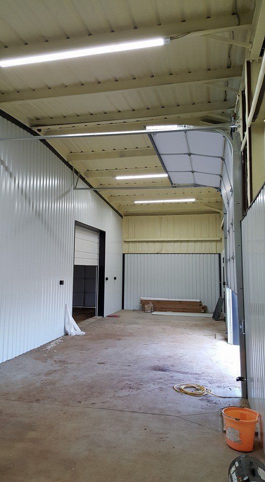 Interior view of a warehouse with white metal walls and ceiling.  Overhead door is partially open, concrete floor.