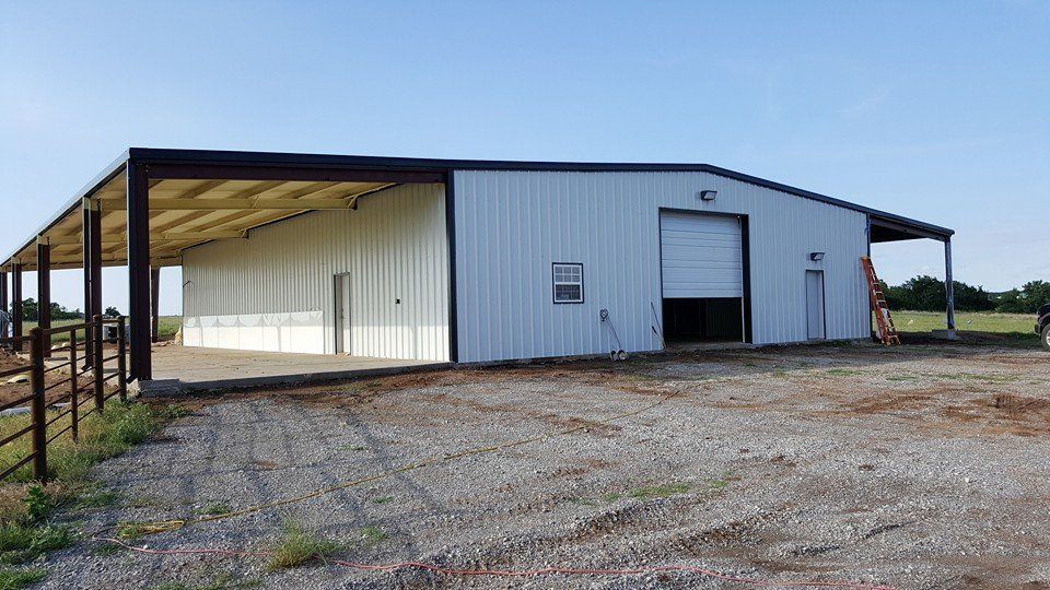 Metal building with attached awning on a gravel lot under a blue sky.