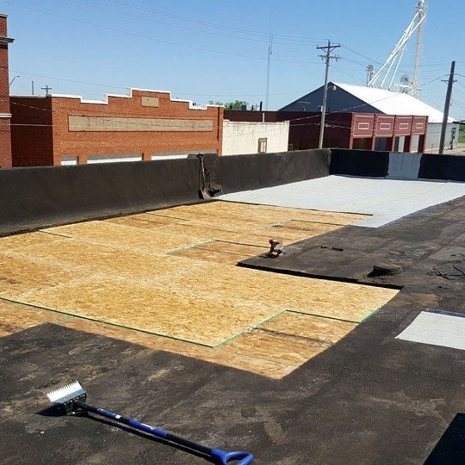 Roof partially covered with plywood and black material; cityscape in the background.