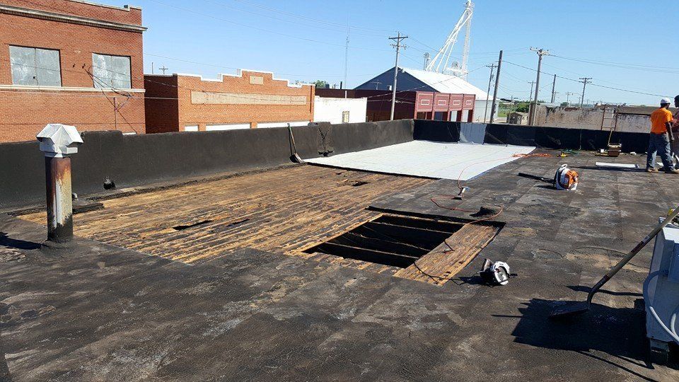 Roof repair in progress; a flat roof with missing sections, tools, and a worker visible in an urban setting.
