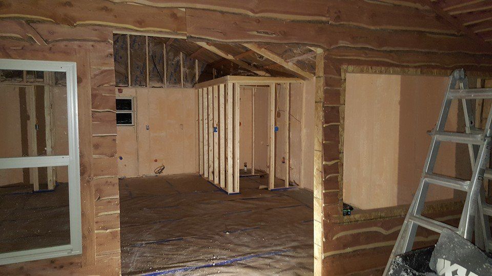Interior view of a building under construction, showing wooden framing, walls, and a ladder.