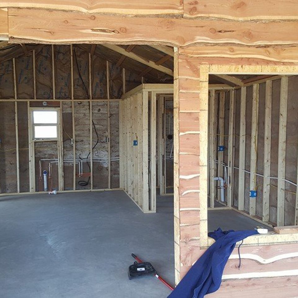 Interior of a building under construction, showing wooden frame, concrete floor, and exposed wiring.
