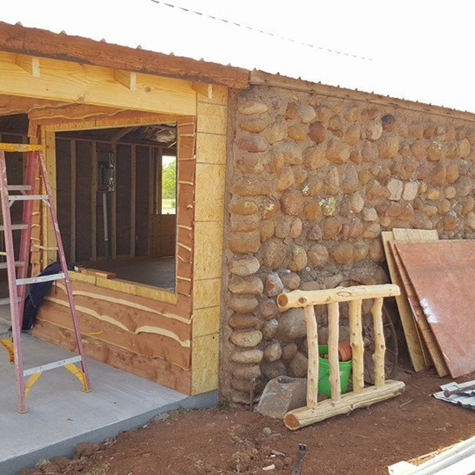Building exterior with stone wall, wood frame, and ladder, under construction.