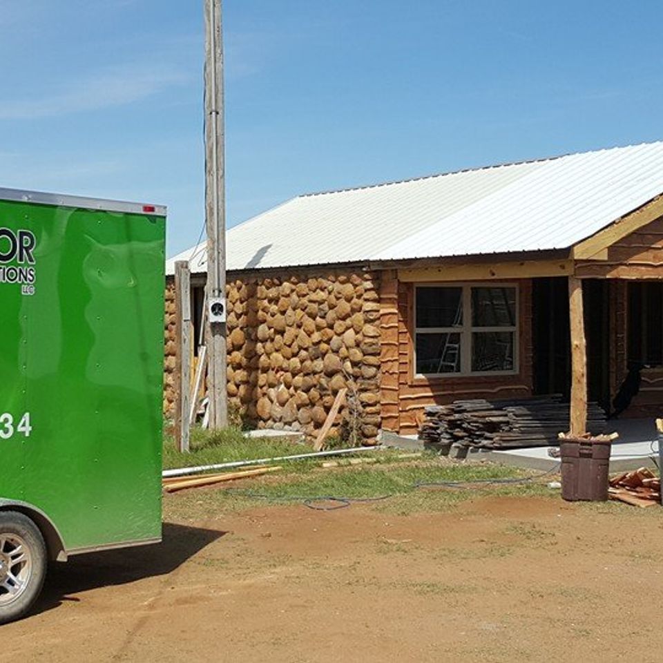 Green trailer next to a house under construction with stone and wood exterior. Bright sunny day.