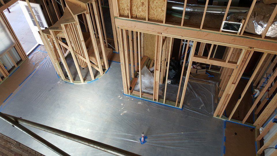Interior view of a building under construction, featuring wooden framing, covered floors, and unfinished walls.