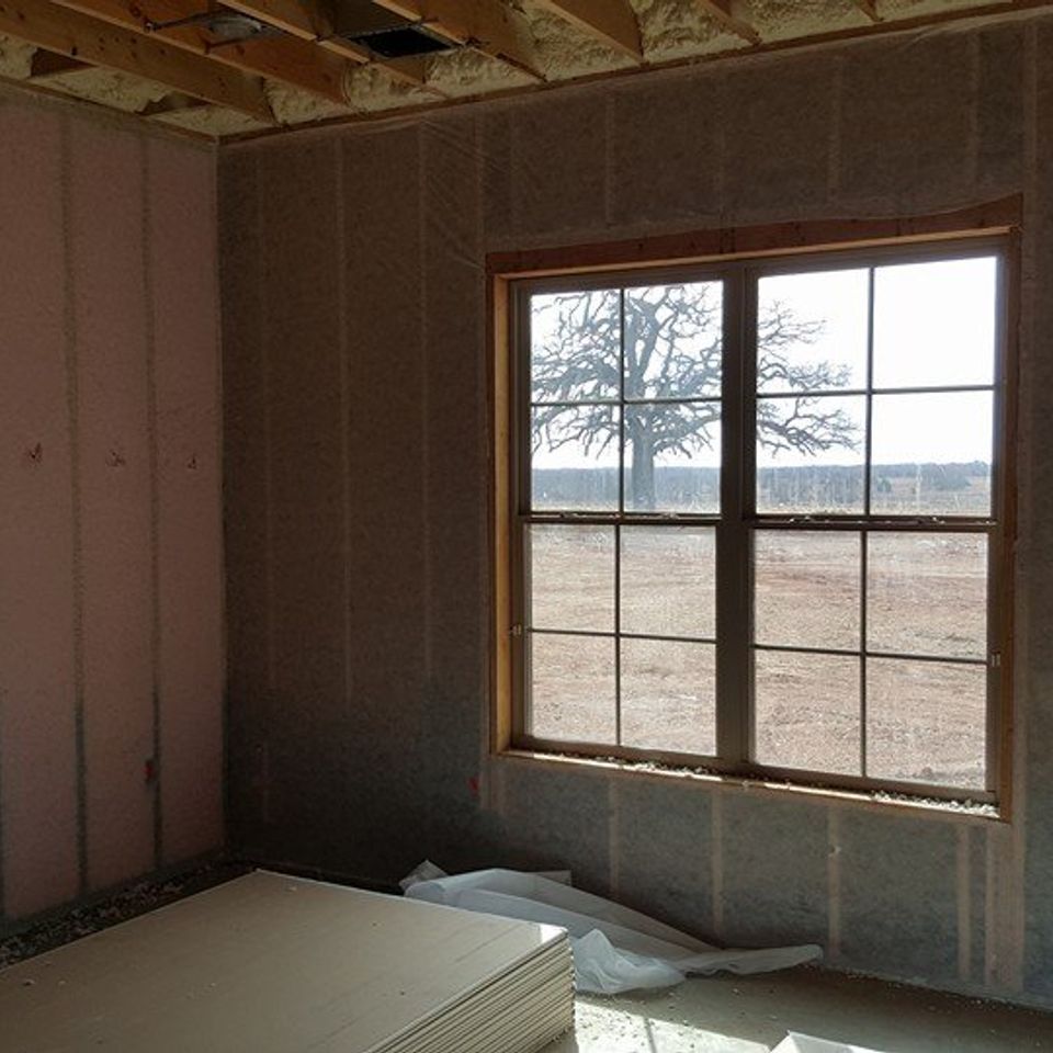 Interior room under construction, with a window overlooking a field and tree. Walls are insulated.