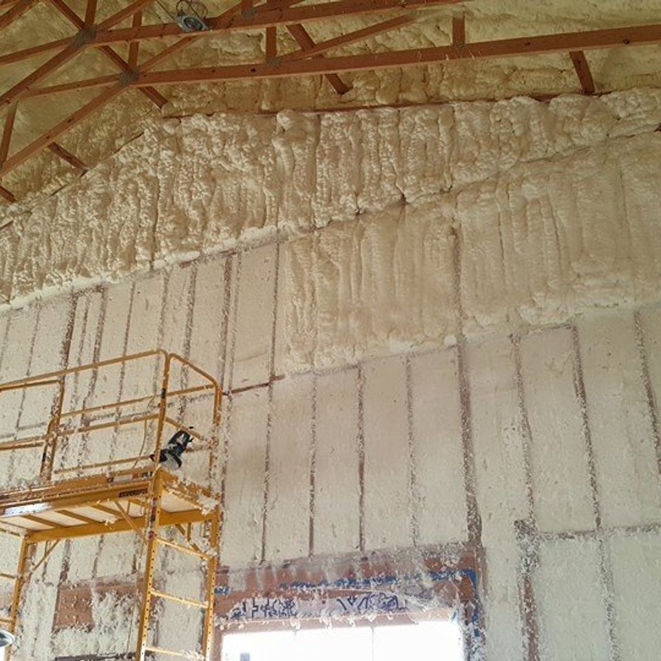 Spray foam insulation on walls and ceiling of a building under construction. A yellow scaffolding stands in front.