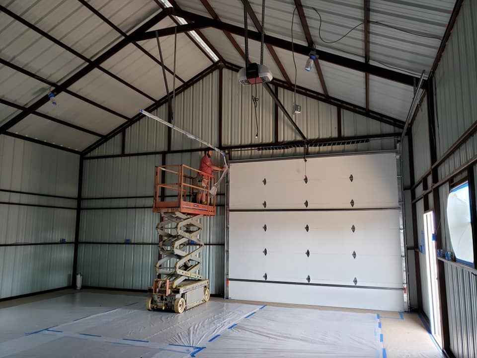 A person on a lift installs a track in a metal-walled garage with the garage door closed.